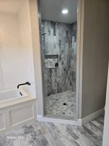 Corner shower tiled in marble-look porcelain next to a drop-in soaking tub