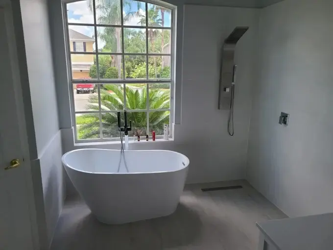 Freestanding soaking tub beneath an arched window in a fully tiled bathroom