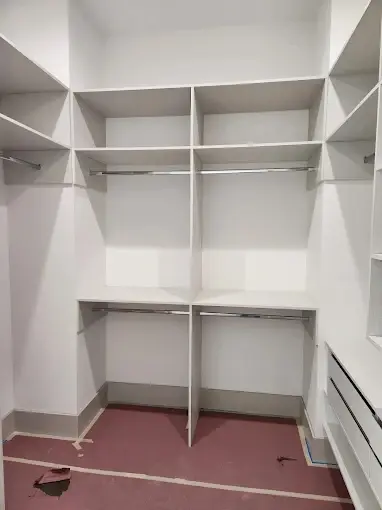 Walk-in closet build-out with white shelving, hanging rods and drawer bank