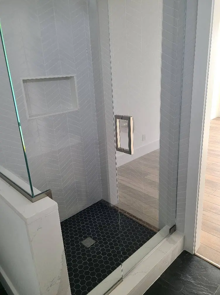 Newly tiled walk-in shower with pebble floor and frameless glass enclosure