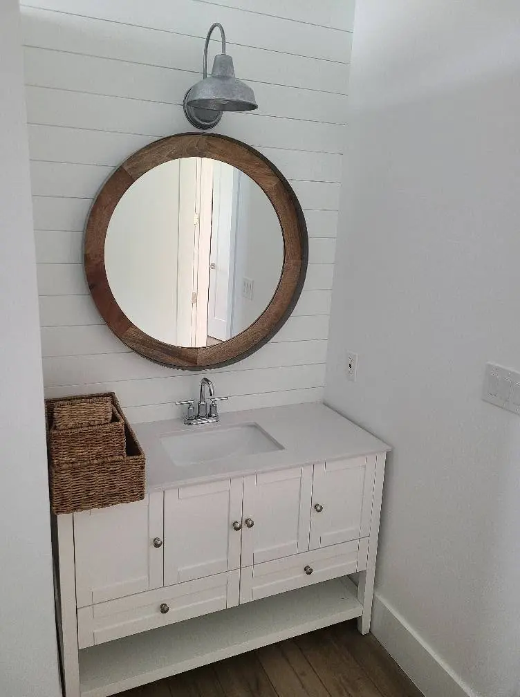 Remodeled guest bathroom with a white shiplap wall, round wood-framed mirror and new vanity