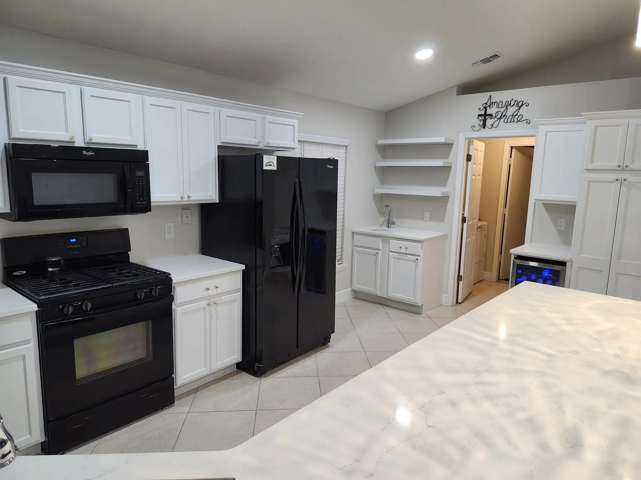 White shaker kitchen cabinets with black appliances and large-format tile flooring